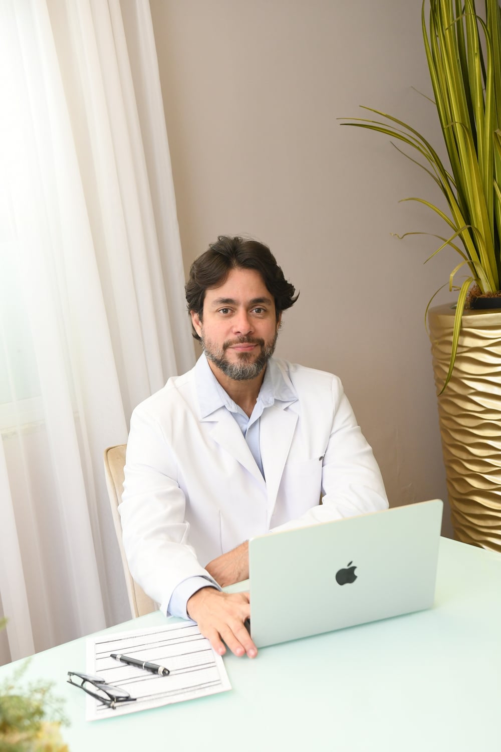 Dr. Pedro Vasconcelos Jr no consultório, com laptop e prancheta de avaliação